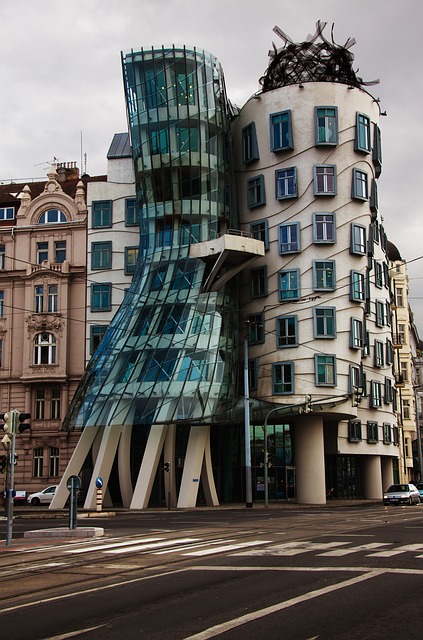 Two buildings of odd proportions. One is glass with concrete supports that seems to be leaning on the neighbor, a concrete building with windows that bulge outward and the building is thicker on the top than the bottom.
