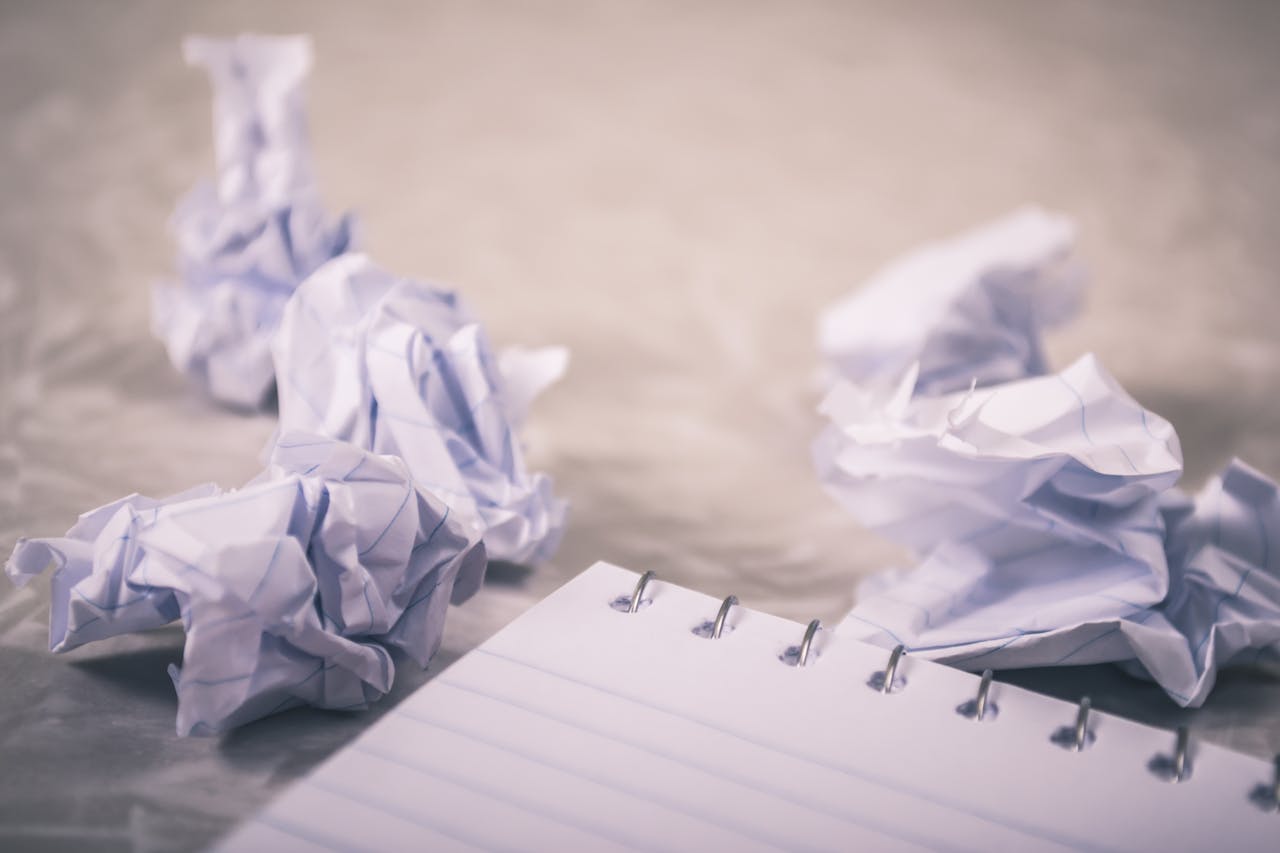 The corner of a notepad on a desk with several crumpled pages nearby