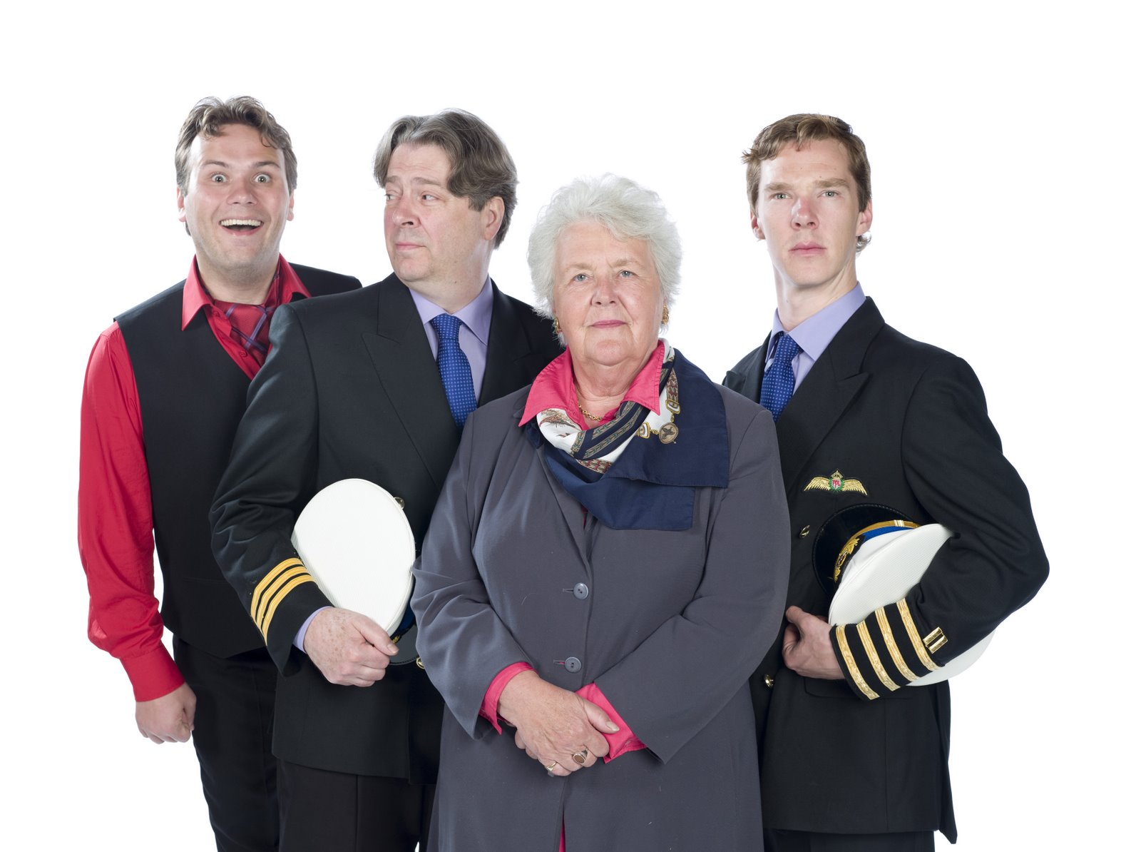Four people in airplane uniforms stand looking at the camera. On the left, a young man in a red shirt and black vest is very excited; next a distinguished middle aged gentleman looks skeptically at him; central-ish is an older woman looking placid; last is a younger man looking noble.