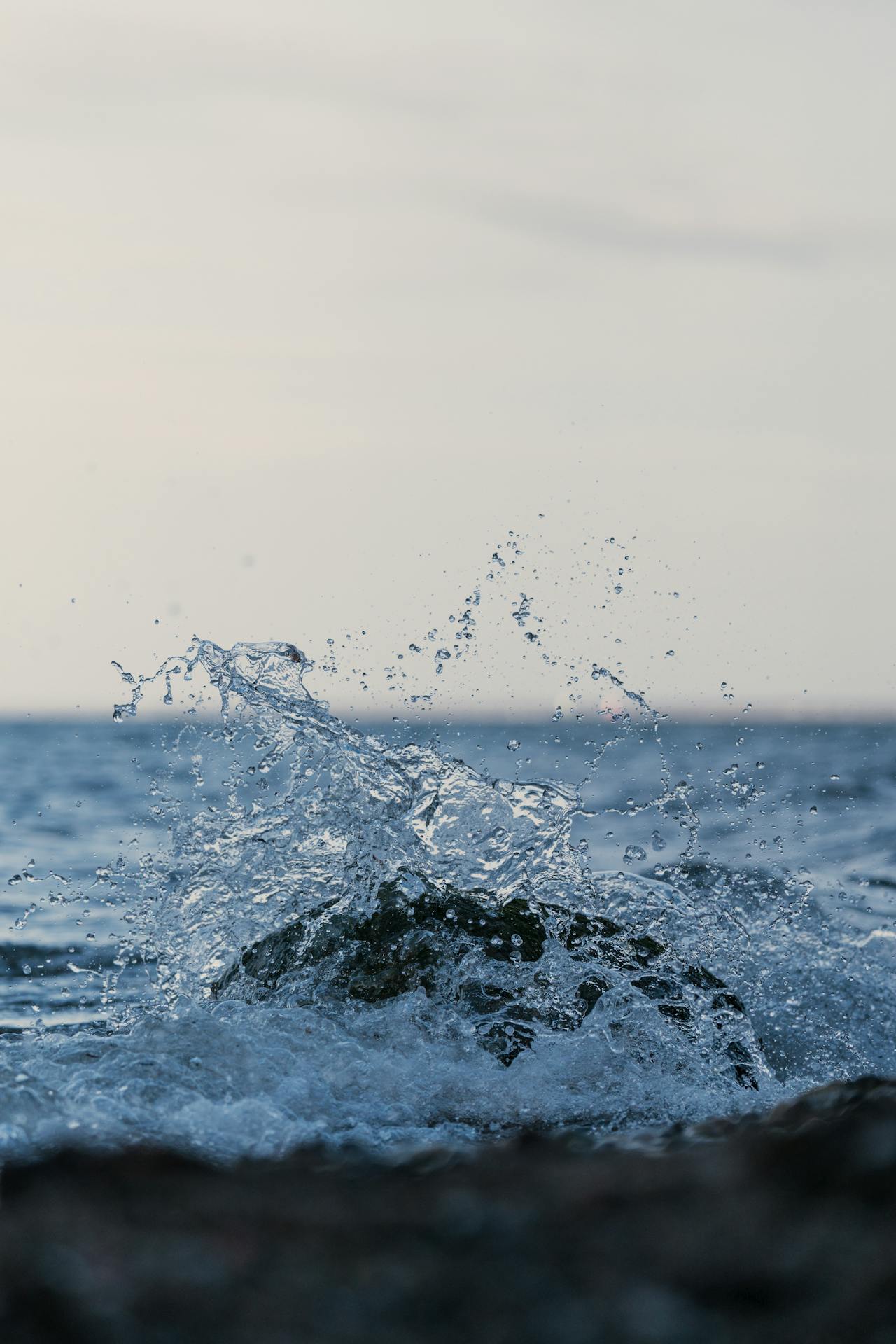 A splash of water in a lake around a smooth object against a pale pink sky